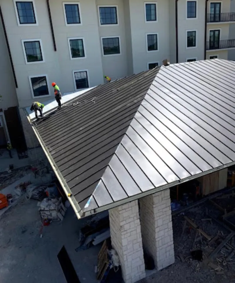 Crew installing standing seam metal roof panels on a commercial project in Timberwood Park